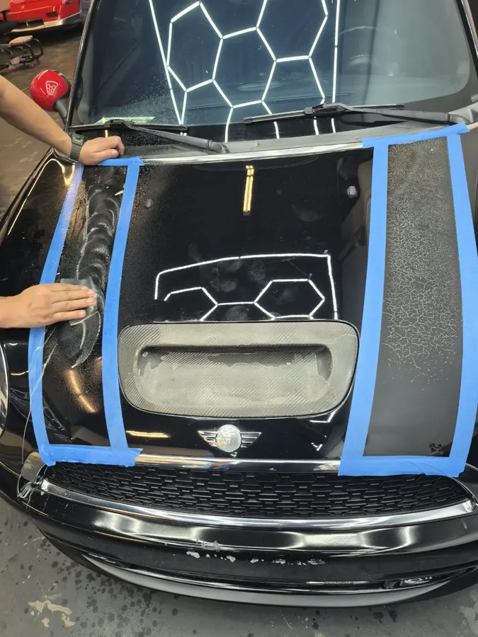 Hands working on a black hood with blue masking tape around surface areas