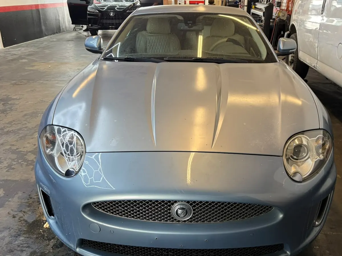 The same light blue Jaguar coupe with clear headlights after restoration