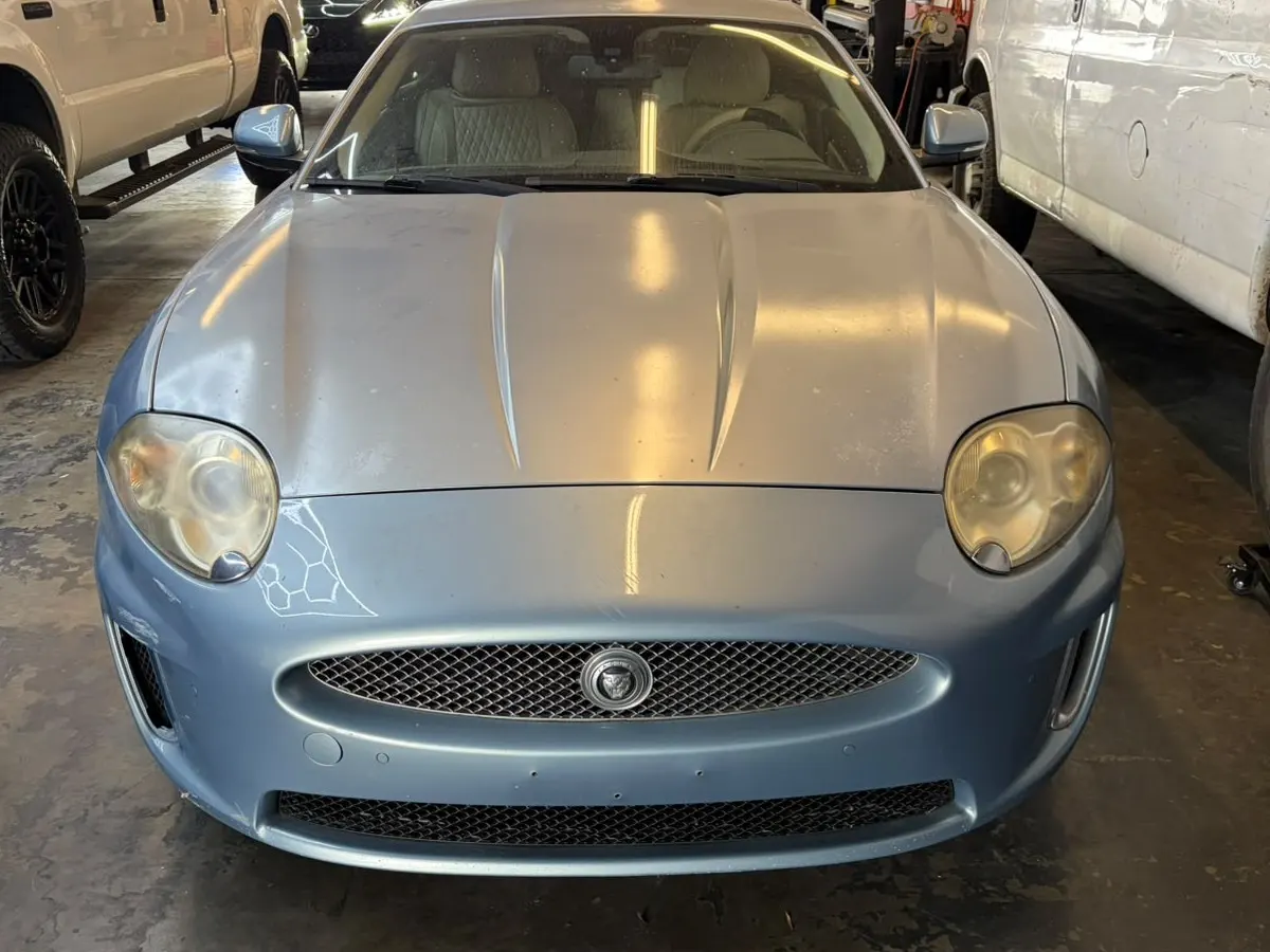 Light blue Jaguar coupe at the Enhanced Automotive shop with cloudy, yellowed headlights