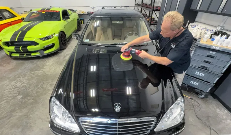 Technician machine-polishing a black Mercedes in the studio